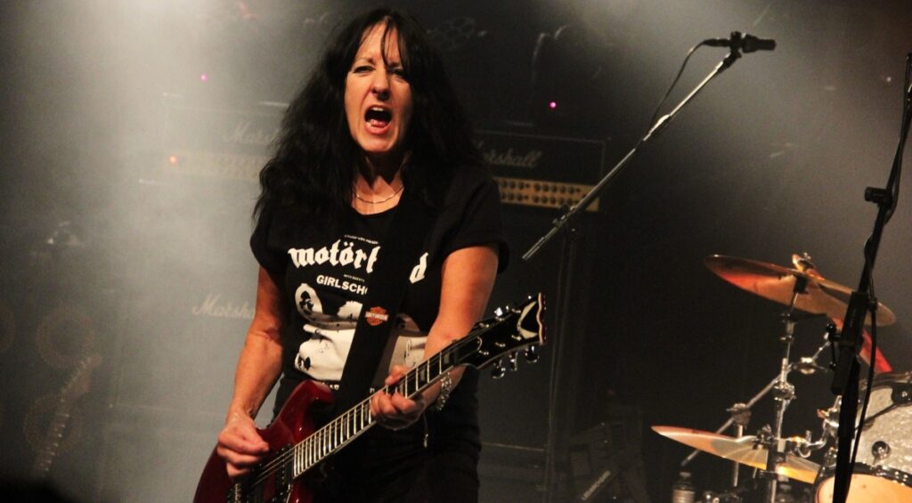 Girlschool Kim McAuliffe, de 65 anos, se apresenta com dificuldades para se manter em pé, cantar e tocar em show em Örebro, na Suécia