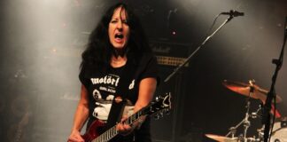 Girlschool Kim McAuliffe, de 65 anos, se apresenta com dificuldades para se manter em pé, cantar e tocar em show em Örebro, na Suécia